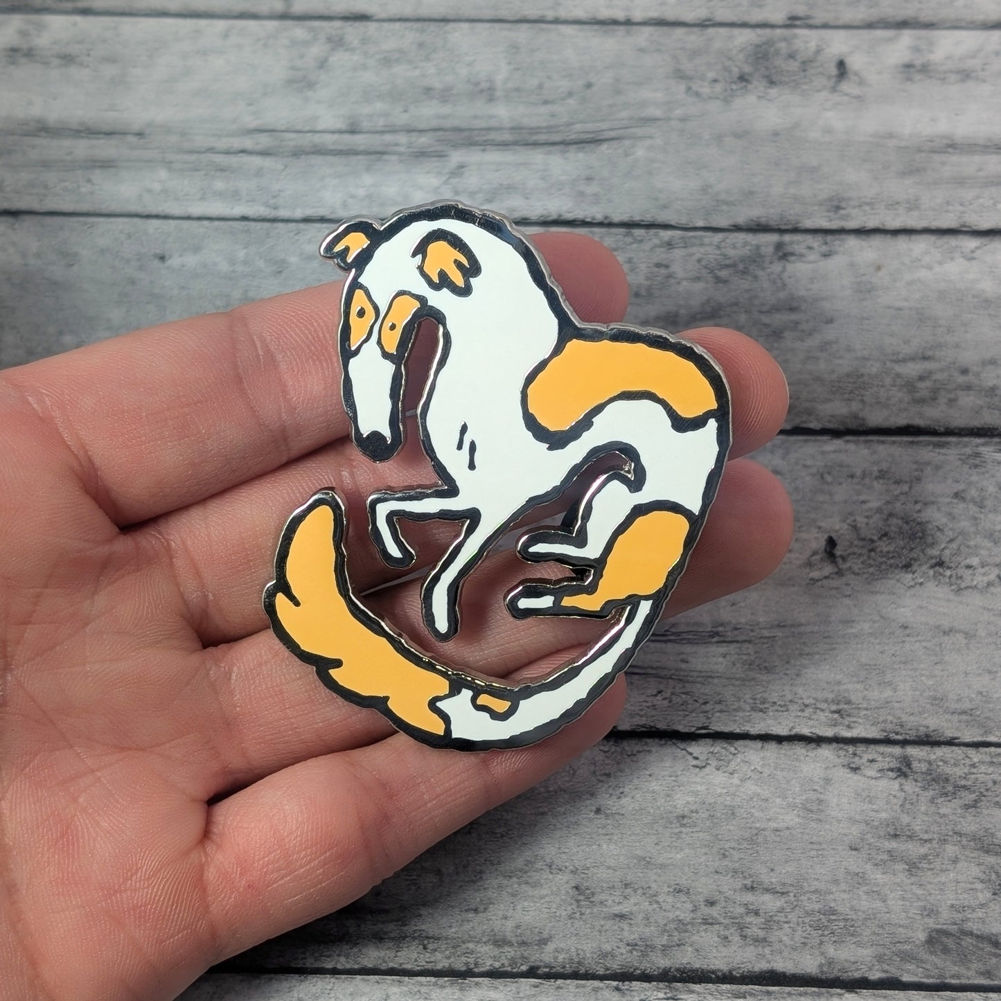 Borzoi enamel pin held in a hand on a wooden surface