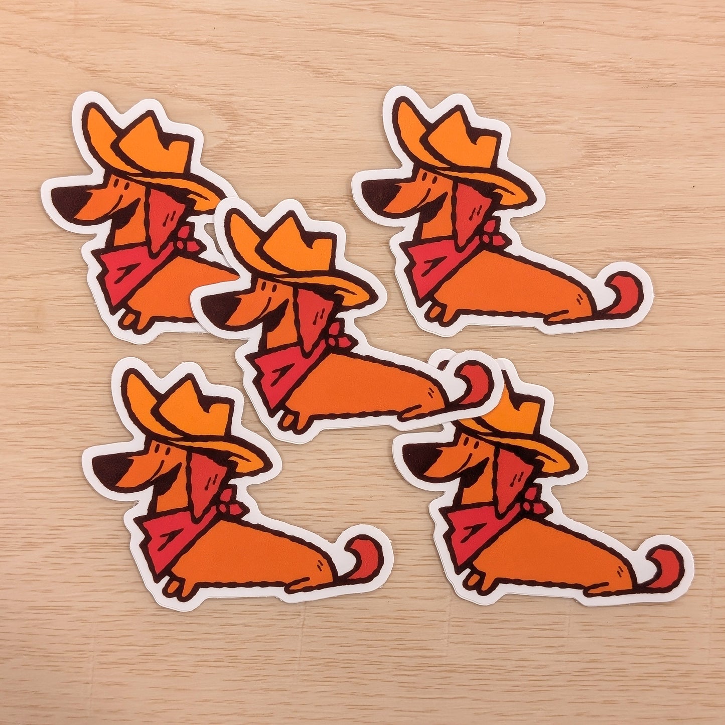 Four orange dachshund stickers with cowboy hats and scarves on a wooden surface.