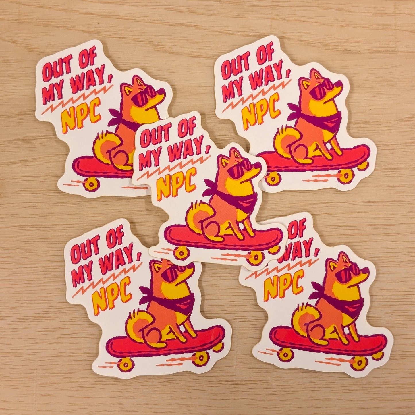 Five stickers with a Shiba Inu dog character on a skateboard and 'Out of My Way, NPC' text on a wooden surface.