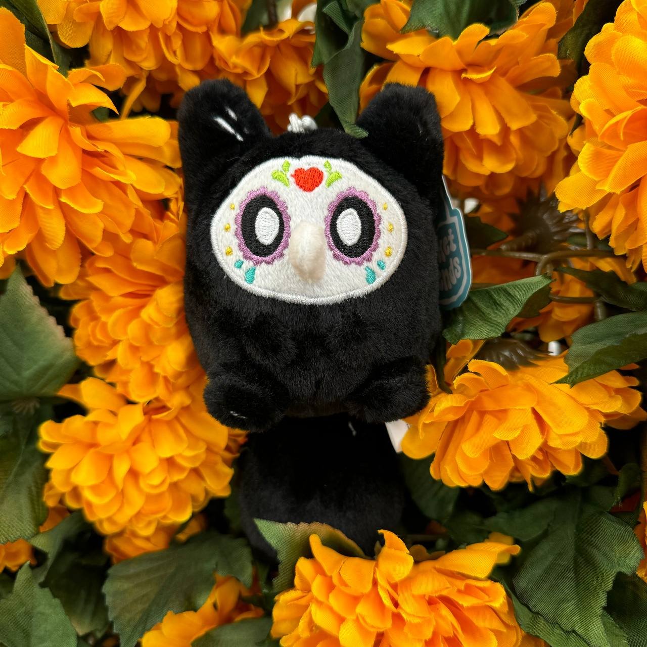 Pocket Friends plush toy in a sugar skull variant, poking out of some flowers.