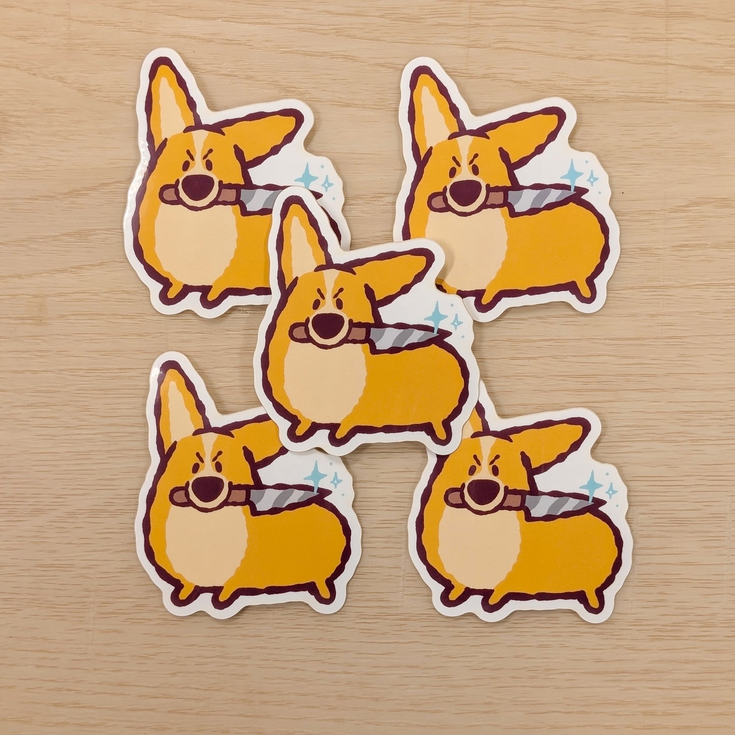 Five stickers of a cartoon corgi holding a knife, on a wooden surface