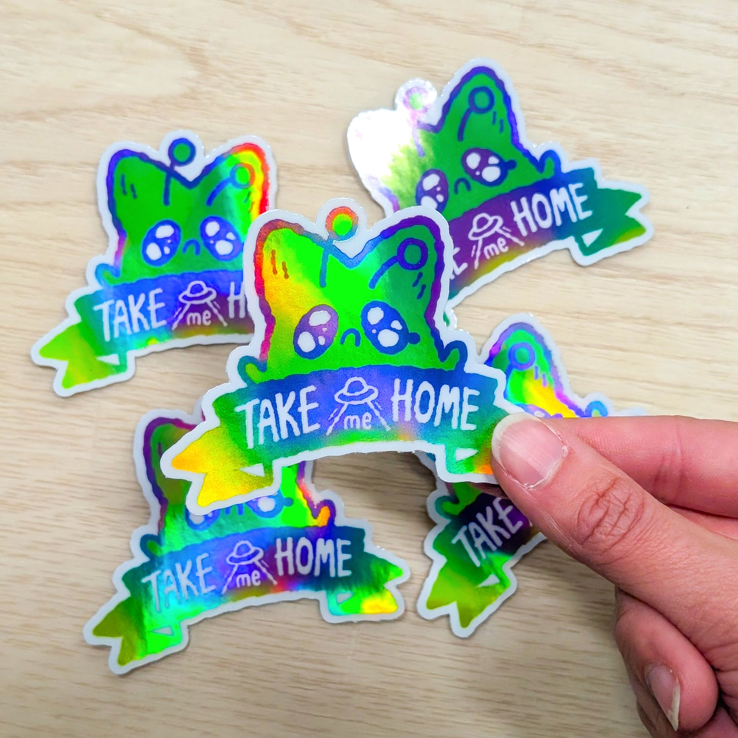 Colorful 'Take Me Home' stickers on a wooden surface with a hand holding one sticker.