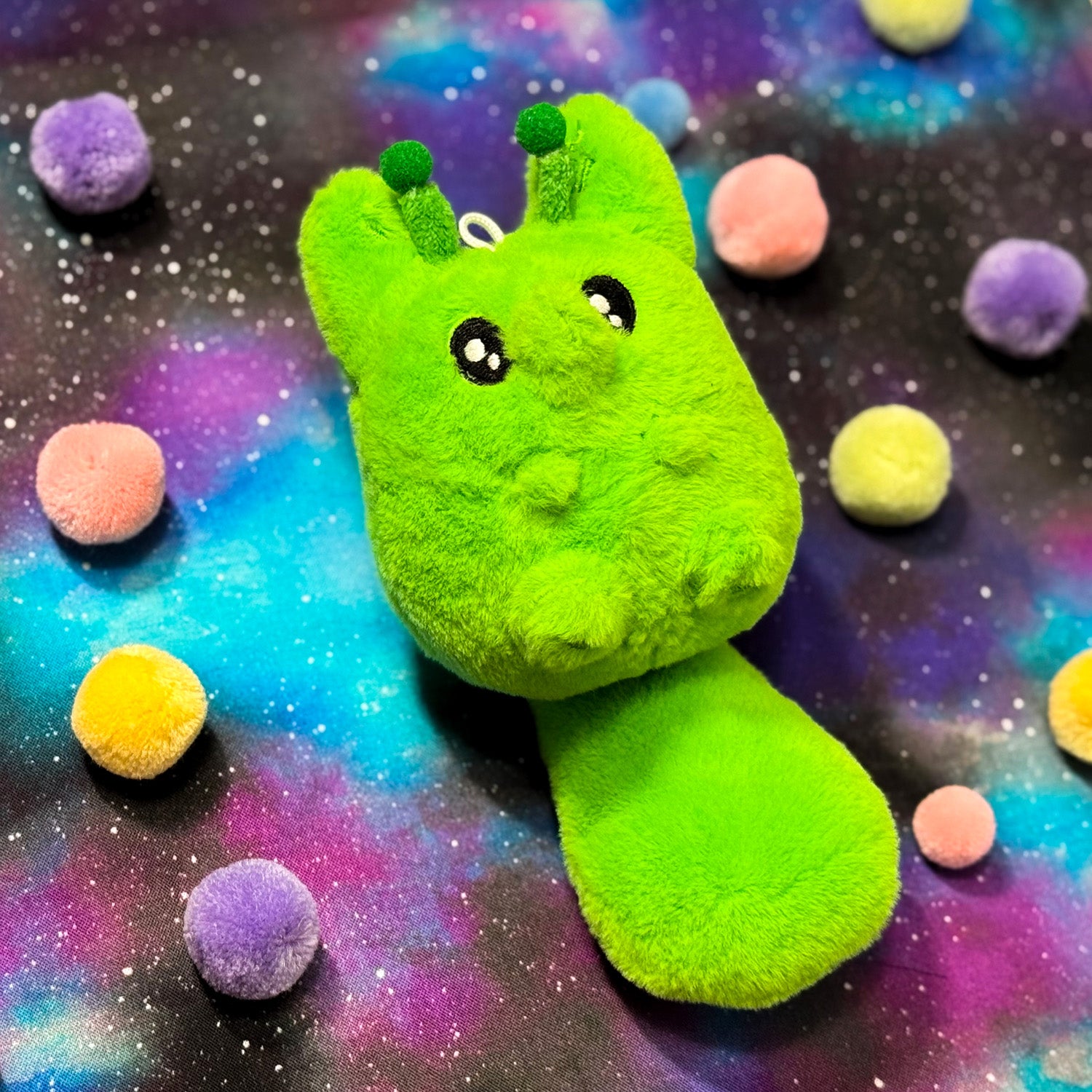 Green alien fox plush toy with a space-themed background featuring colorful planets.
