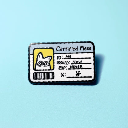Enamel pin with a design resembling a 'Certified Mess' badge on a light blue background