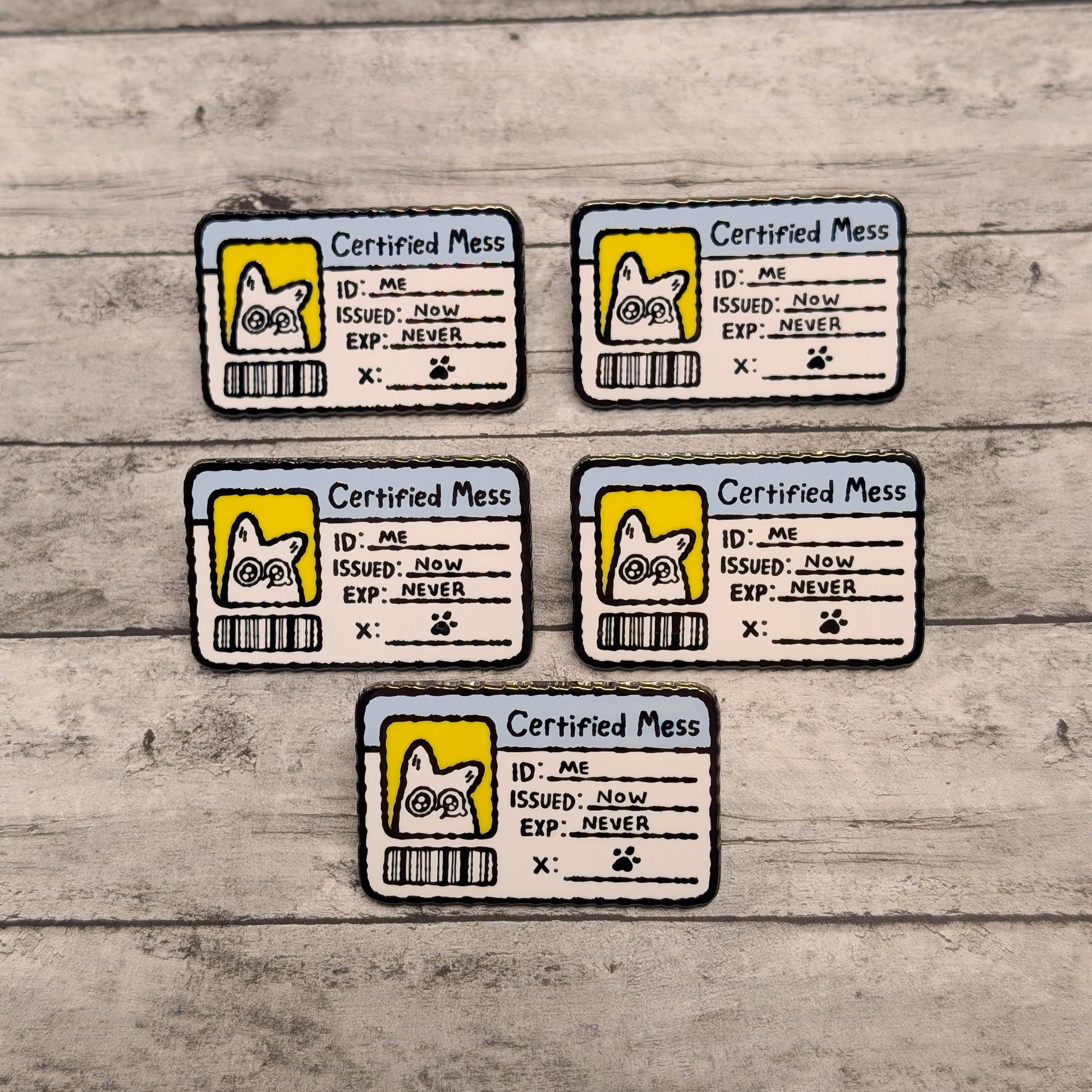 Five 'Certified Mess' enamel pins with cartoon white fox designs on a wooden surface.