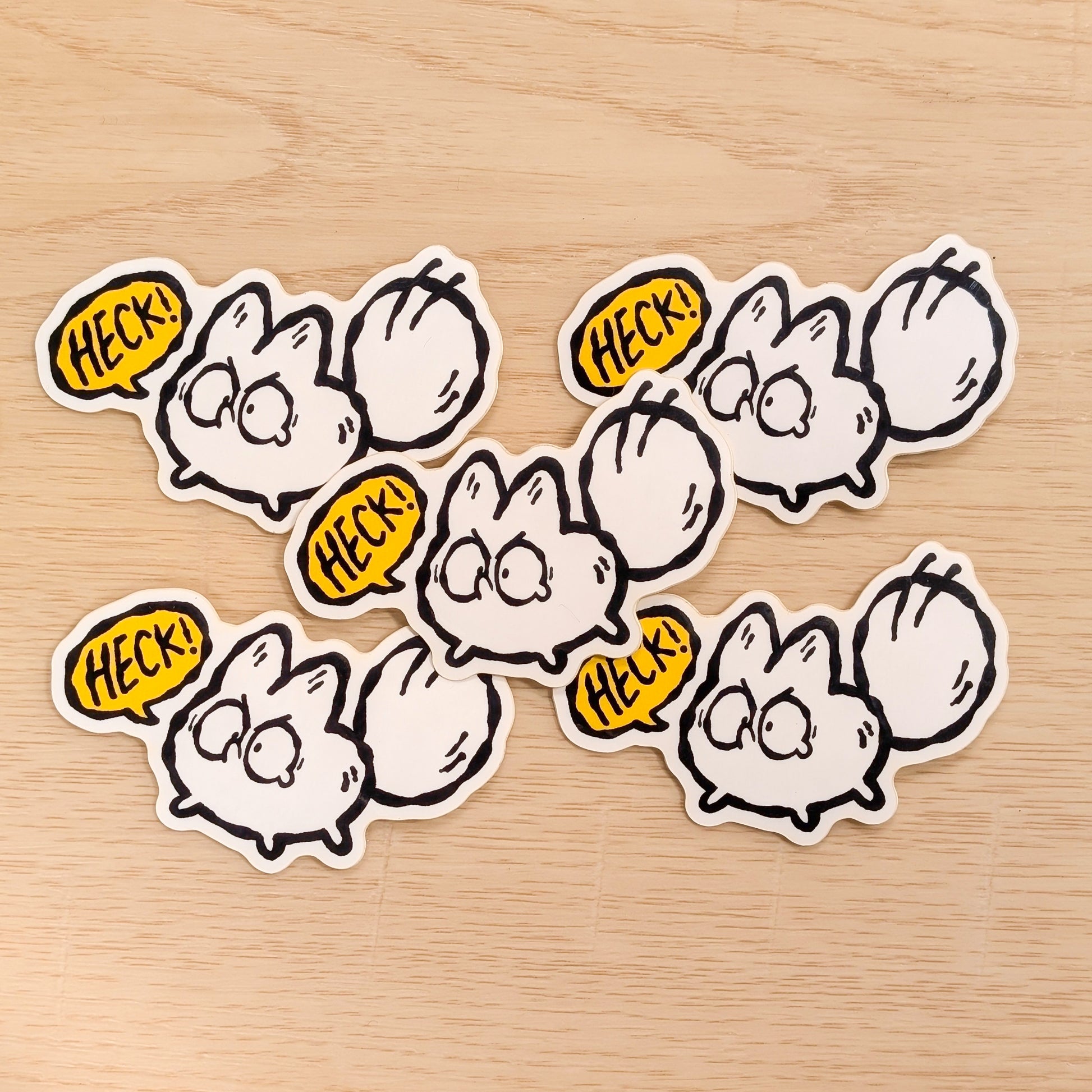 Set of six cartoon-style white fox stickers with speech bubbles saying 'HECK!' on a wooden surface.
