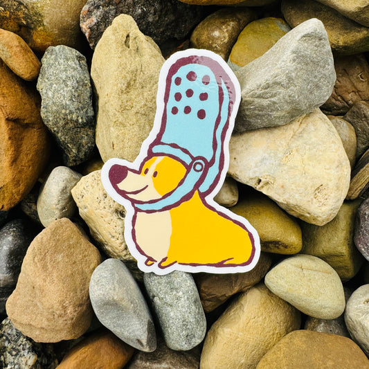 Cartoon corgi sticker with a blue croc hat on a bed of multicolored stones