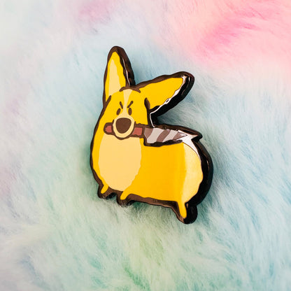 Enamel pin of a cartoon corgi holding a knife on a fluffy, multicolored background