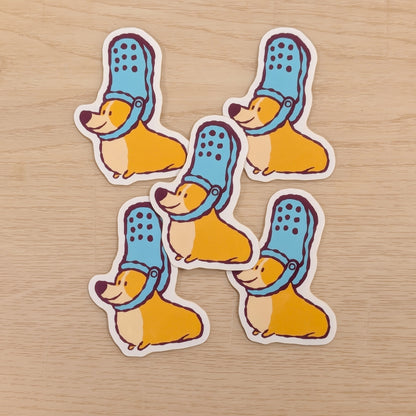 Five stickers of corgis wearing blue shoes on their heads, on a wooden surface