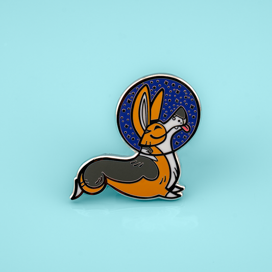 Enamel pin with a stylized corgi wearing a space helmet, on a light blue background