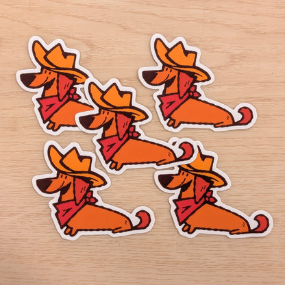 Four orange dachshund stickers with cowboy hats and scarves on a wooden surface.