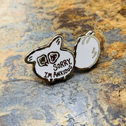 Enamel pin with a white fox design and 'Sorry, I'm Anxious' text on a stone background