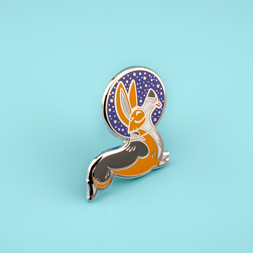 Enamel pin with a stylized corgi wearing a space helmet, on a light blue background
