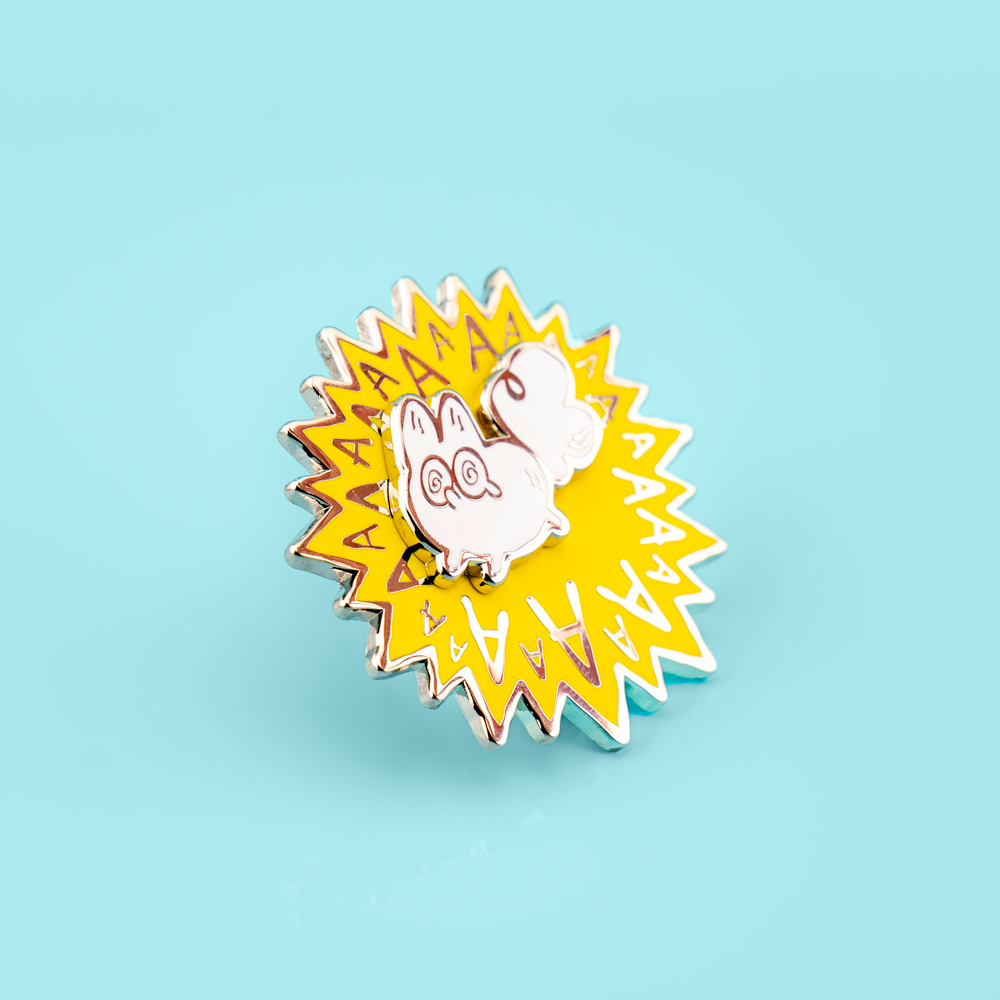 Enamel pin with a cartoon white fox and 'AA' text on a light blue background