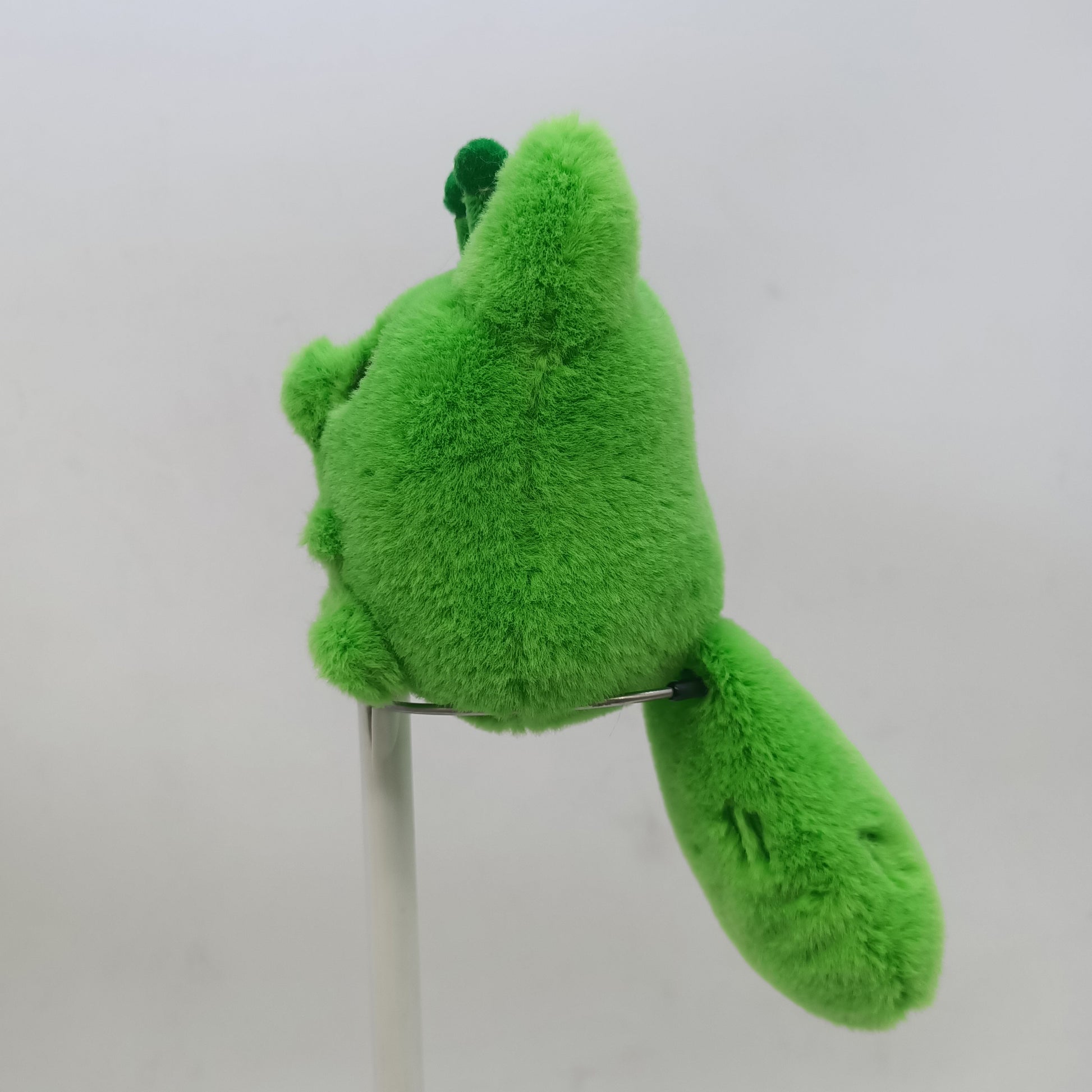 Green alien fox plush toy on a stand against a white background