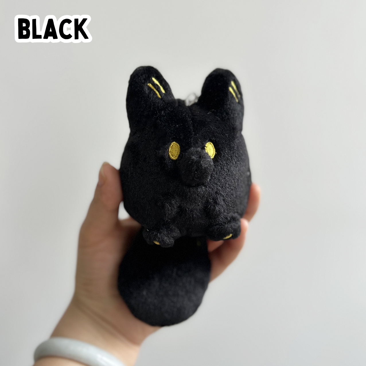 A hand holding a mini black fox plush toy against a white background