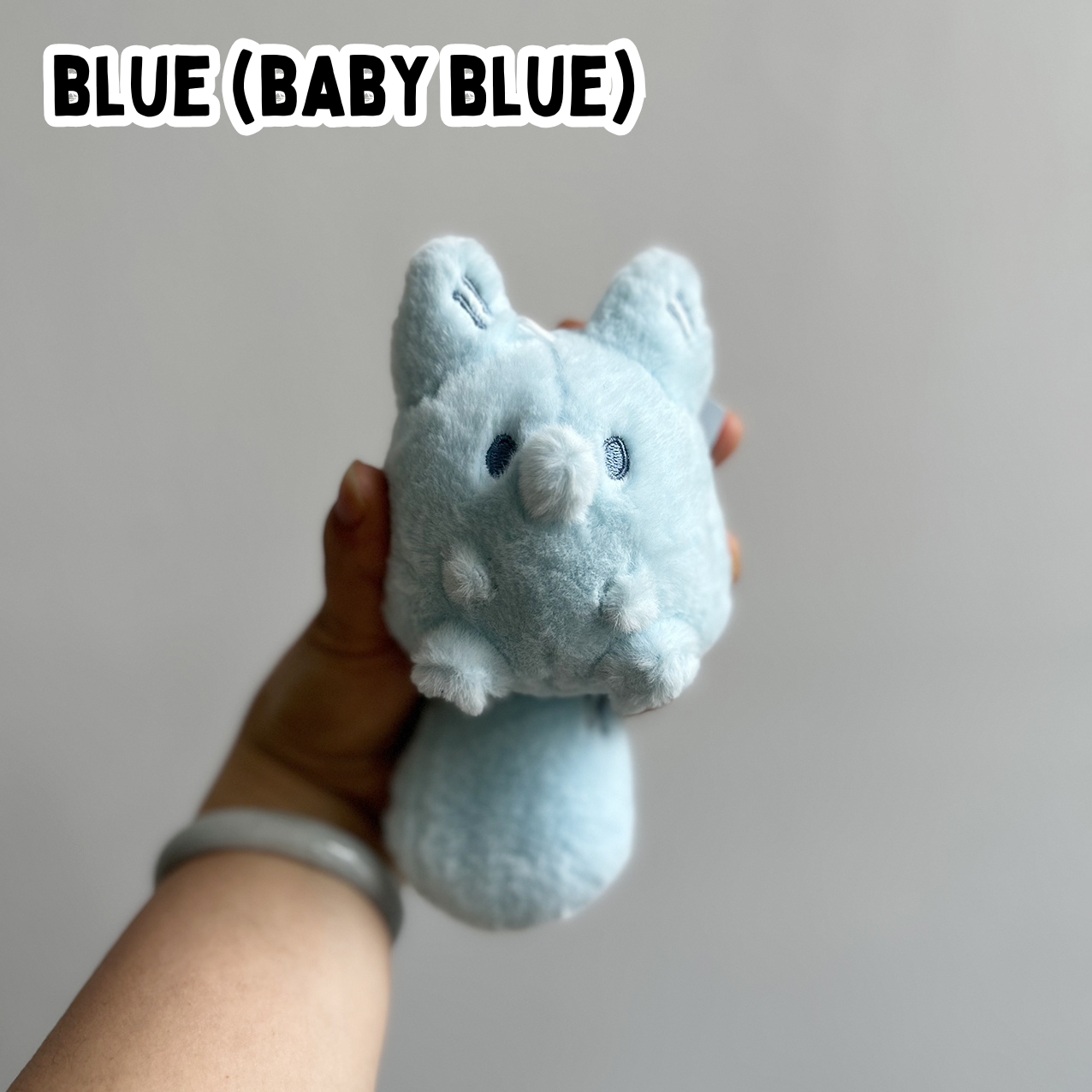 A hand holding a mini blue fox plush toy against a white background