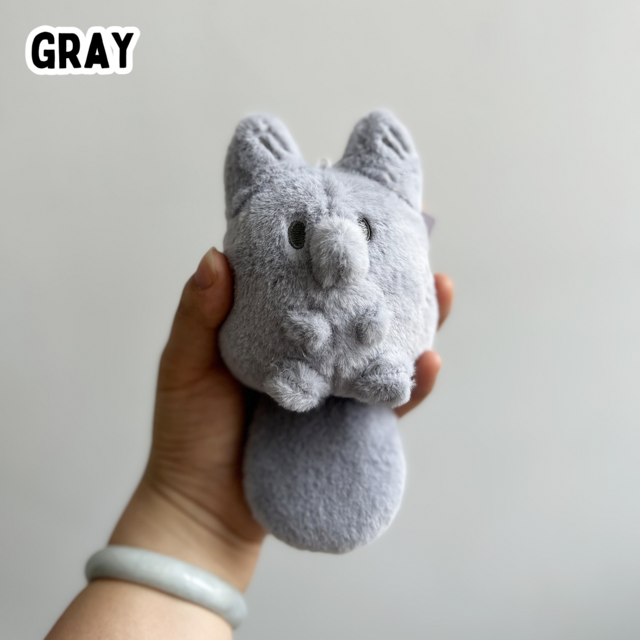 A hand holding a mini gray fox plush toy against a white background