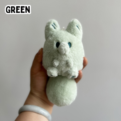 A hand holding a mini green fox plush toy against a white background