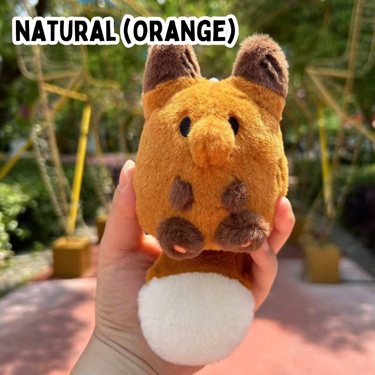 A hand holding a mini orange fox plush toy against a natural background