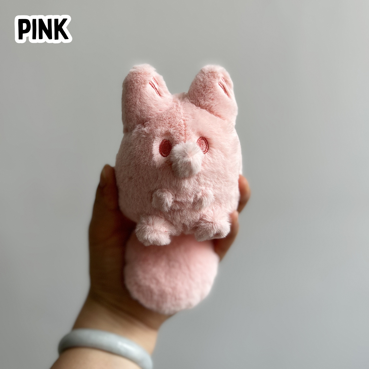 A hand holding a mini pink fox plush toy against a white background