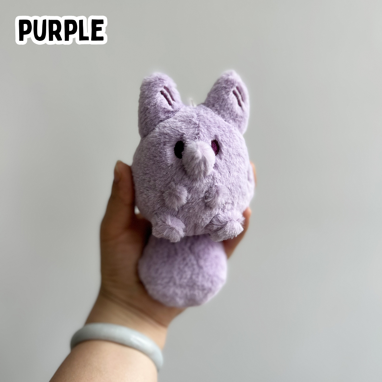 A hand holding a mini purple fox plush toy against a white background