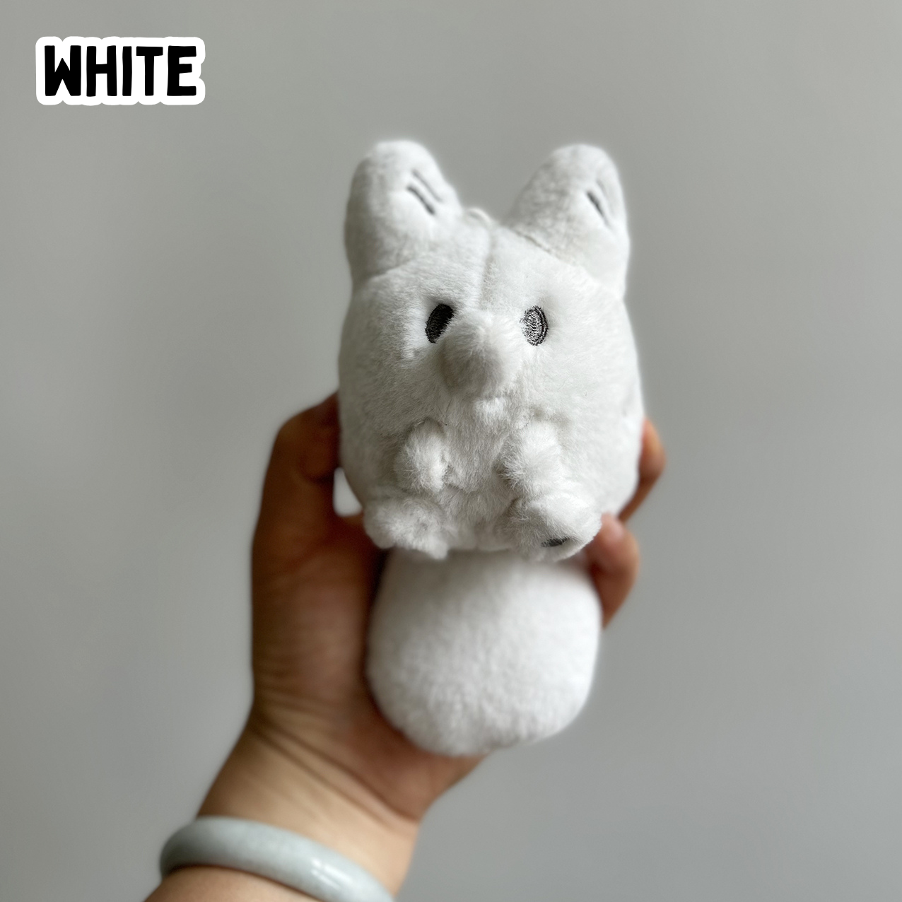 A hand holding a mini white fox plush toy against a white background
