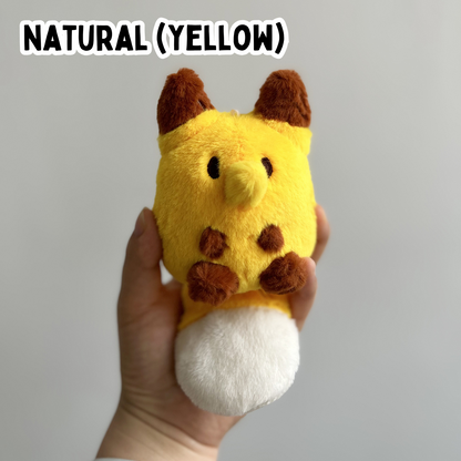 A hand holding a mini yellow fox plush toy against a white background