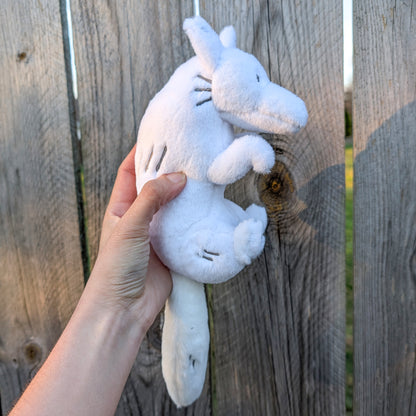 A hand holding a plush toy of a white wolf, with a wooden fence in the background