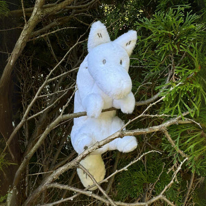 A white wolf plush toy holding onto some branches in a bush