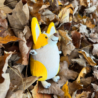 Plush toy of a corgi lying in a pile of fall leaves