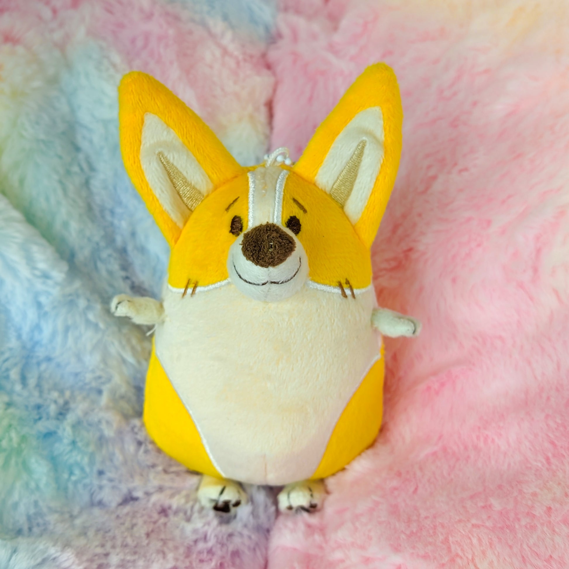 Plush toy of a corgi lying on a pastel rainbow blanket