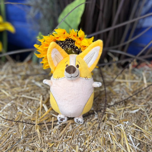 Small corgi plush toy that is sitting infront of a flower.