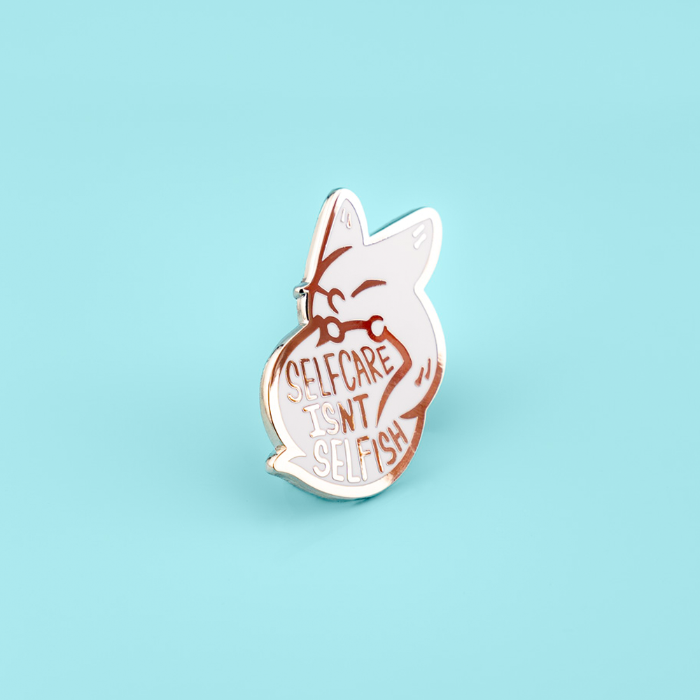 Pin with white fox design and 'Selfcare isn't selfish' text on a light blue background