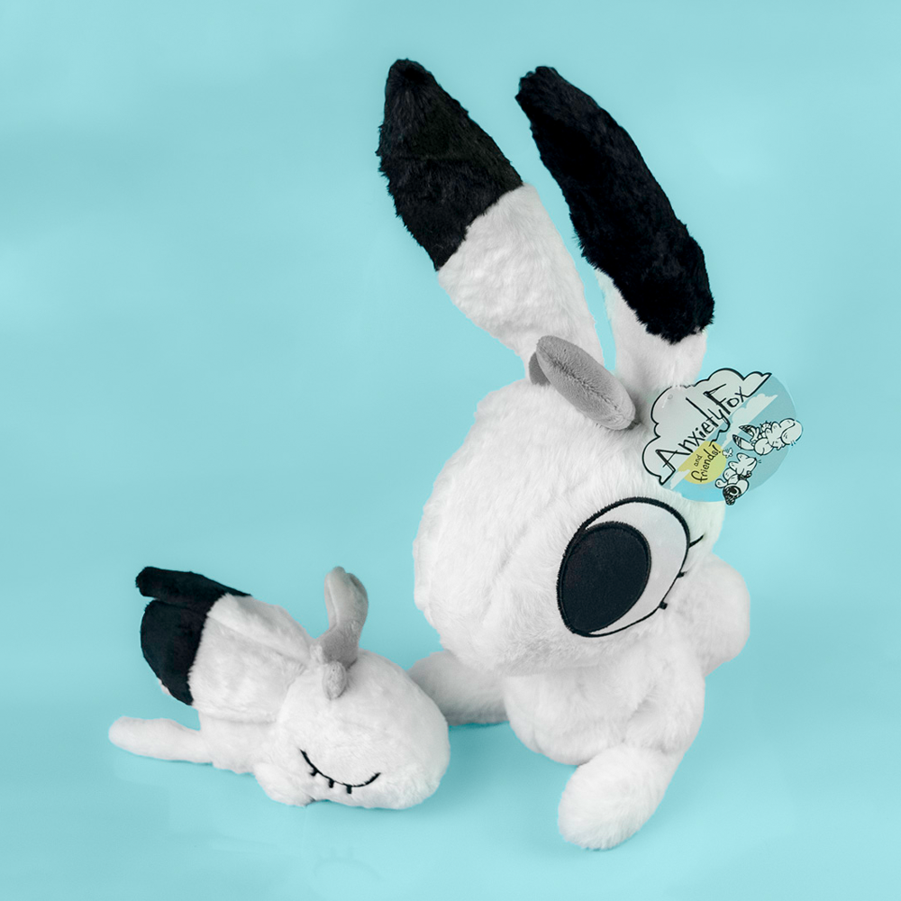 Two plush toys of white rabbits with black accents, against a light blue background