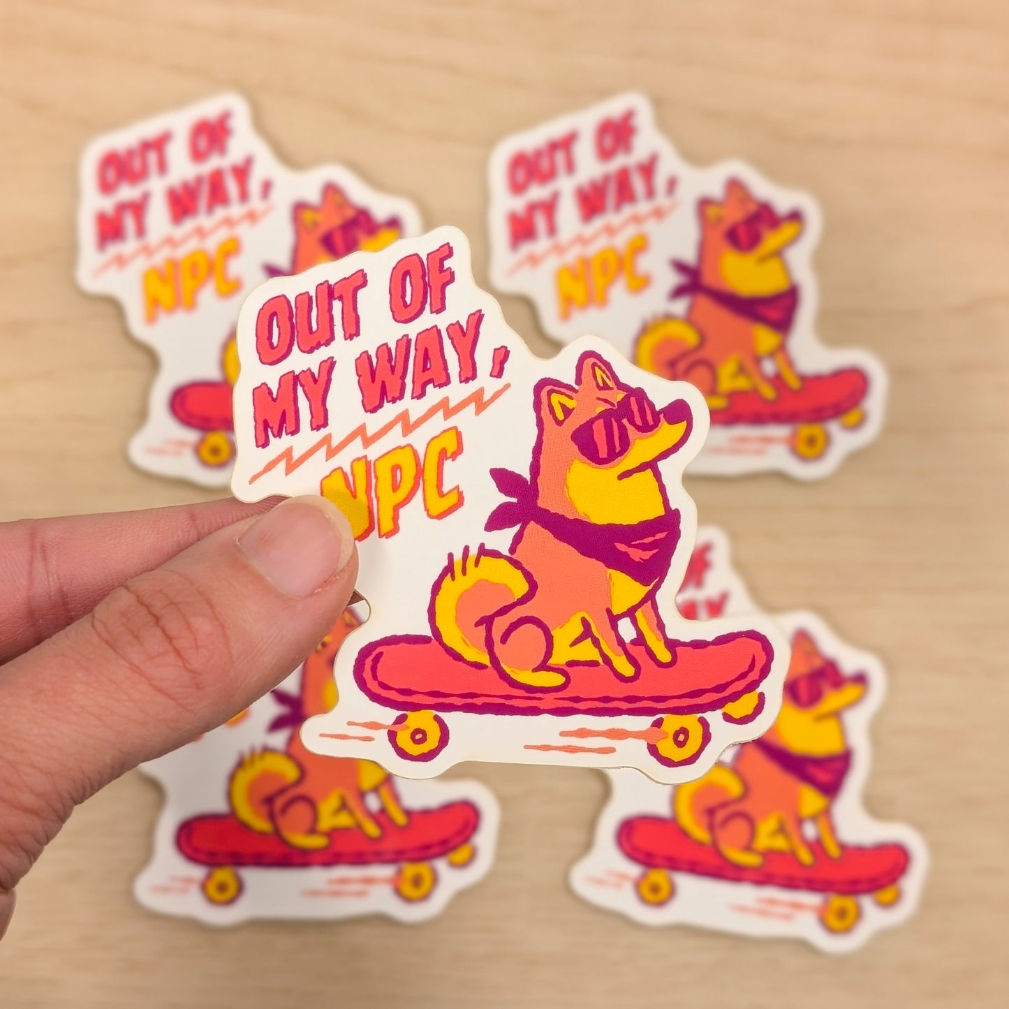 Sticker with a Shiba Inu on a skateboard and 'Out of My Way, VPC' text held by a hand on a beige background