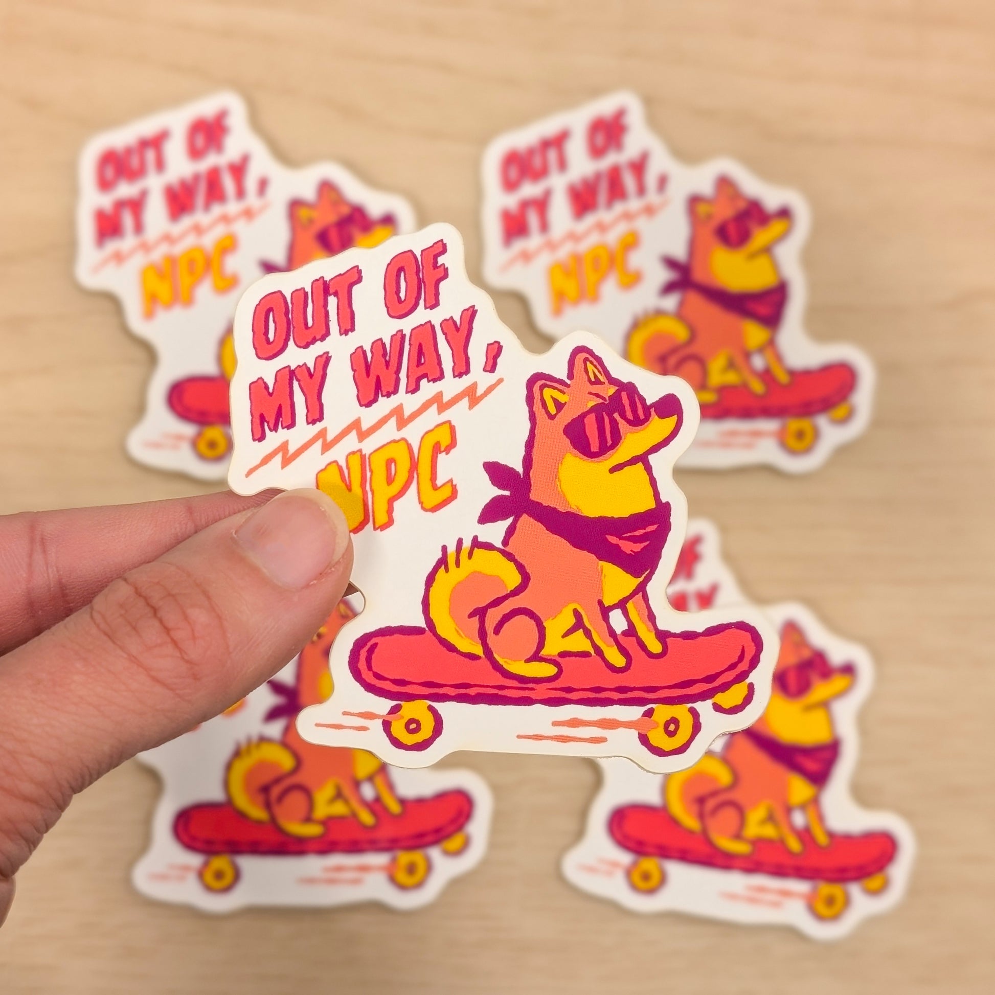 Sticker with a Shiba Inu on a skateboard and 'Out of My Way, VPC' text held by a hand on a beige background