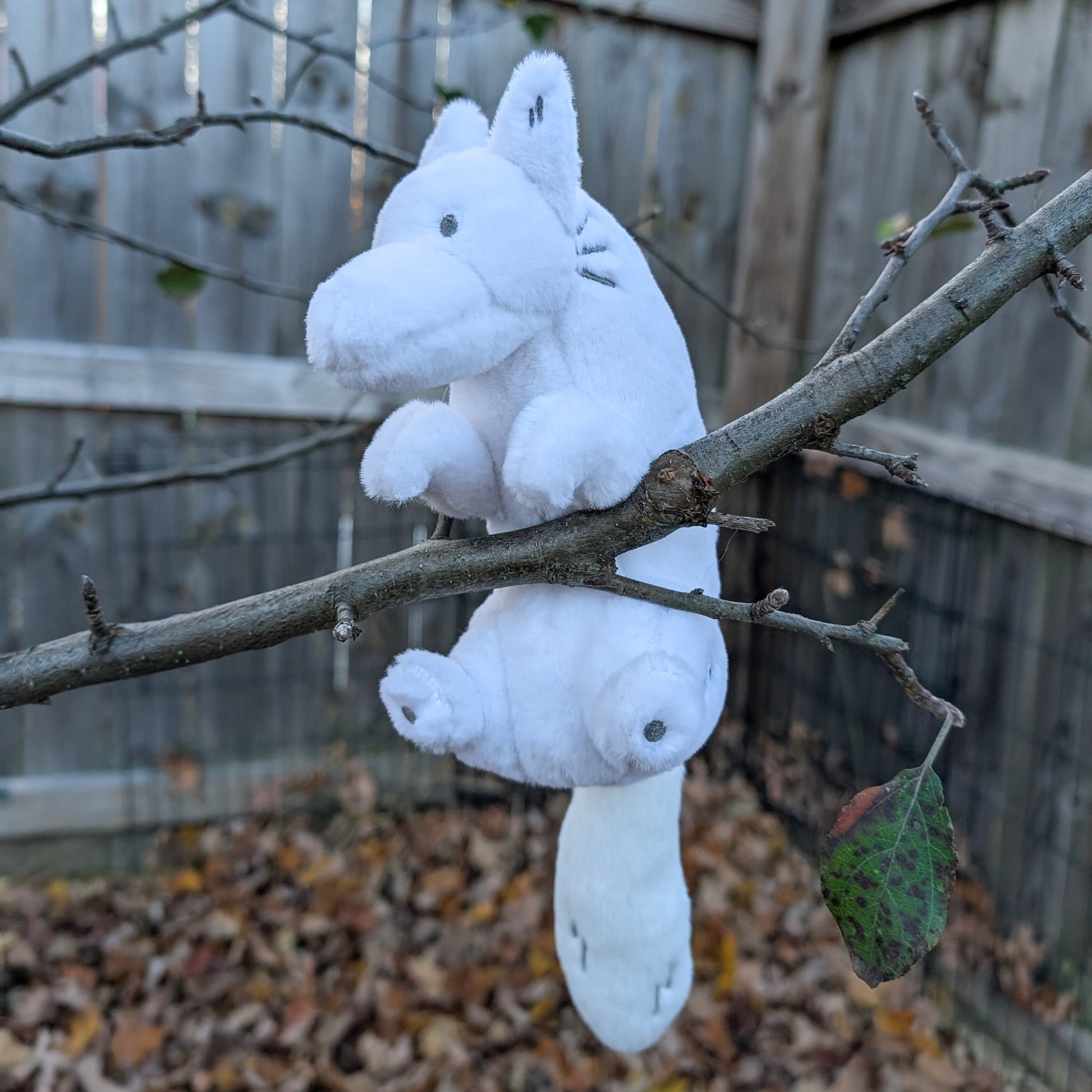 Plush toy of a white wolf sitting in a tree
