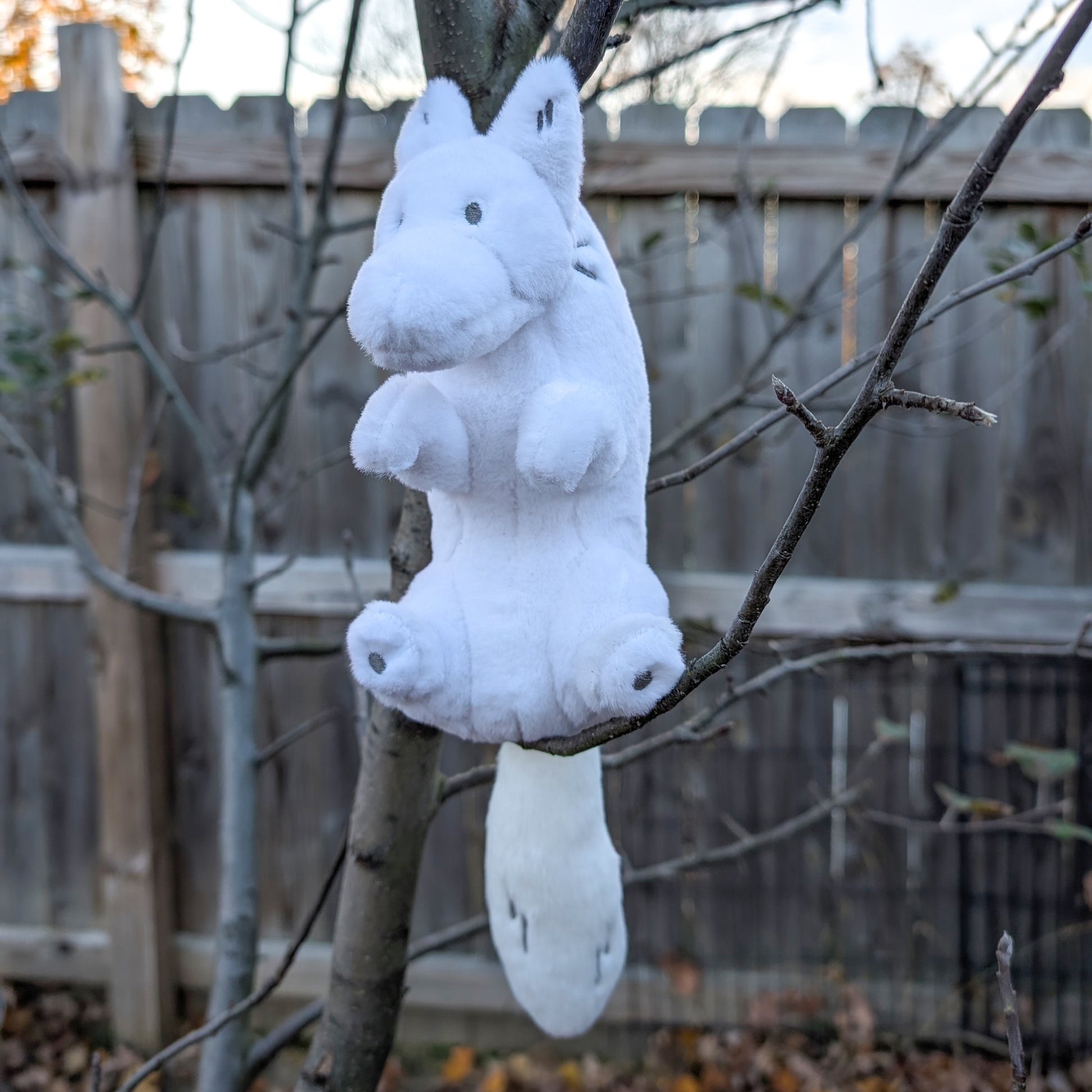 A plush toy of a white wolf sitting in a tree