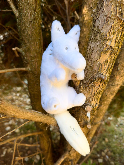 A plush toy of a white wolf sitting in a tree