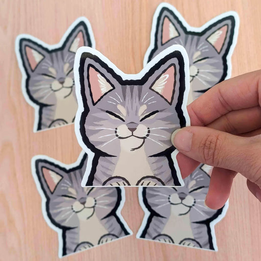 Grey tabby cat vinyl sticker by Made By Nao! features a playful peeker design, perfect for decorating laptops, notebooks, or water bottles.